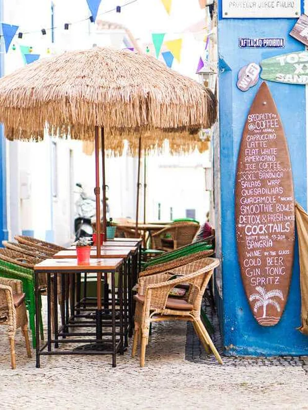 Outdoor café seating under straw umbrellas in a Portuguese village street