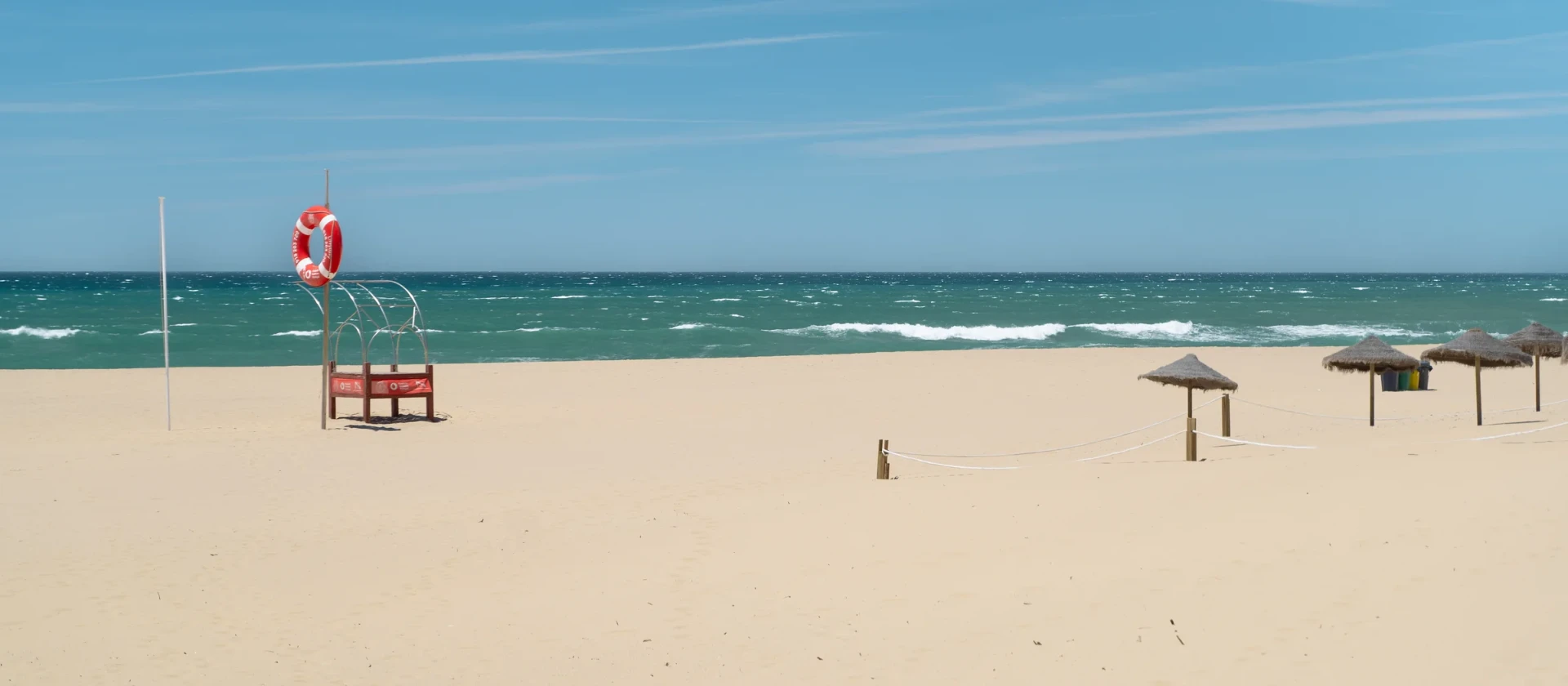Sandy Atlantic beach with turquoise water and straw umbrellas near Carvoeira